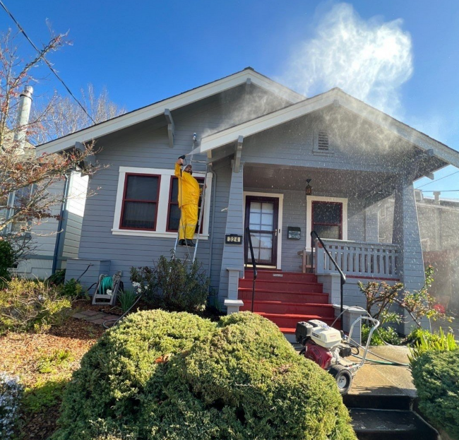 A Man in a Yellow Raincoat Washing the Front of a House.