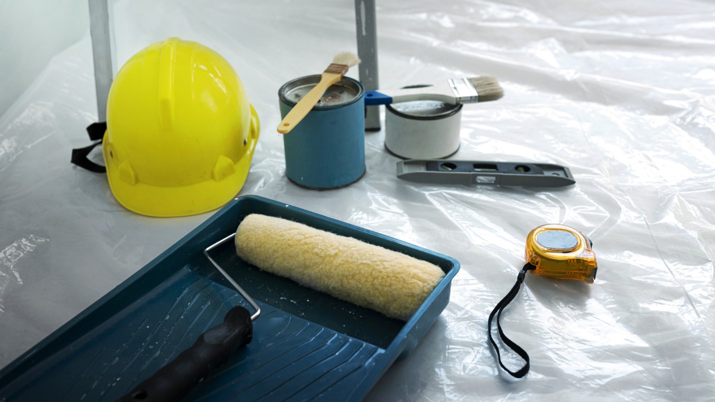 Various Painting Supplies Sit Out on a Plastic Drop Cloth, Including Paint Brushes and Cans.