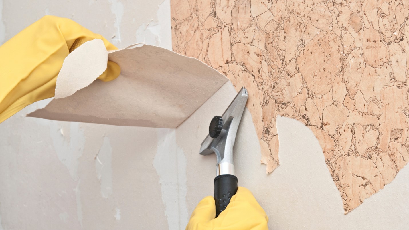 Hands Wearing Yellow Gloves Use a Scrapper to Remove Wallpaper.