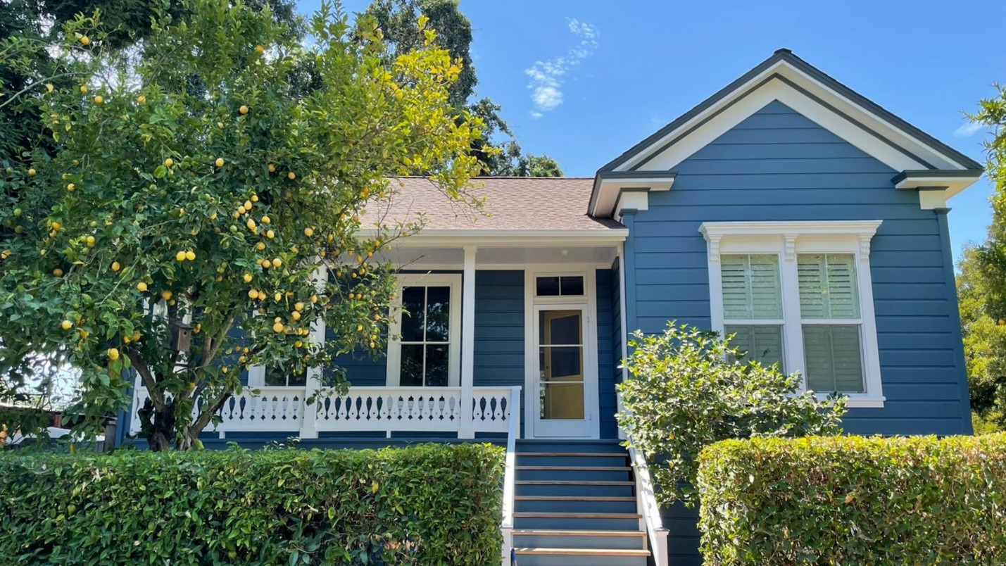 A Blue House With White Trim and a Ripe Fruit Tree Growing in the Front Yard.