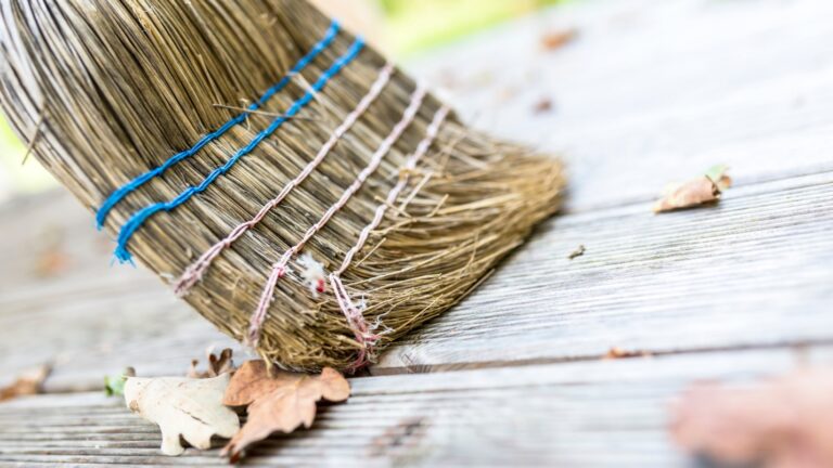 Close up of a broom sweeping fall leaves from a wooden deck