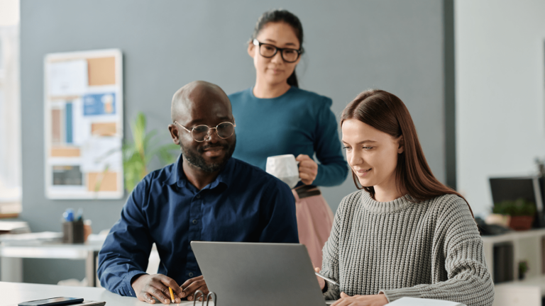 Office workers sit together at a table working on laptops