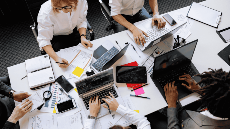 Office workers sit together at a table working on laptops