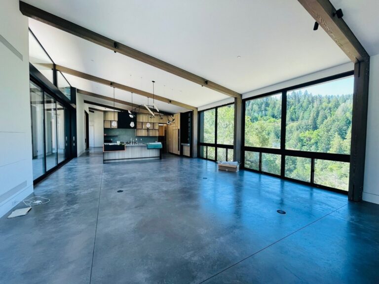 A sleek open-concept living room with white walls and dark beams.