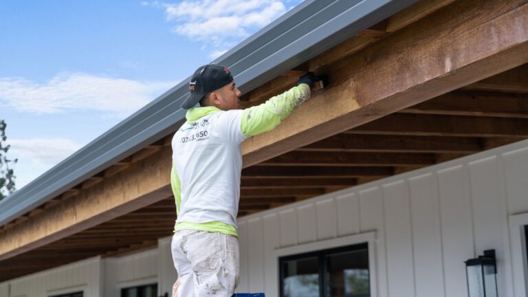 A housepainter stains the wooden beams outside of a home