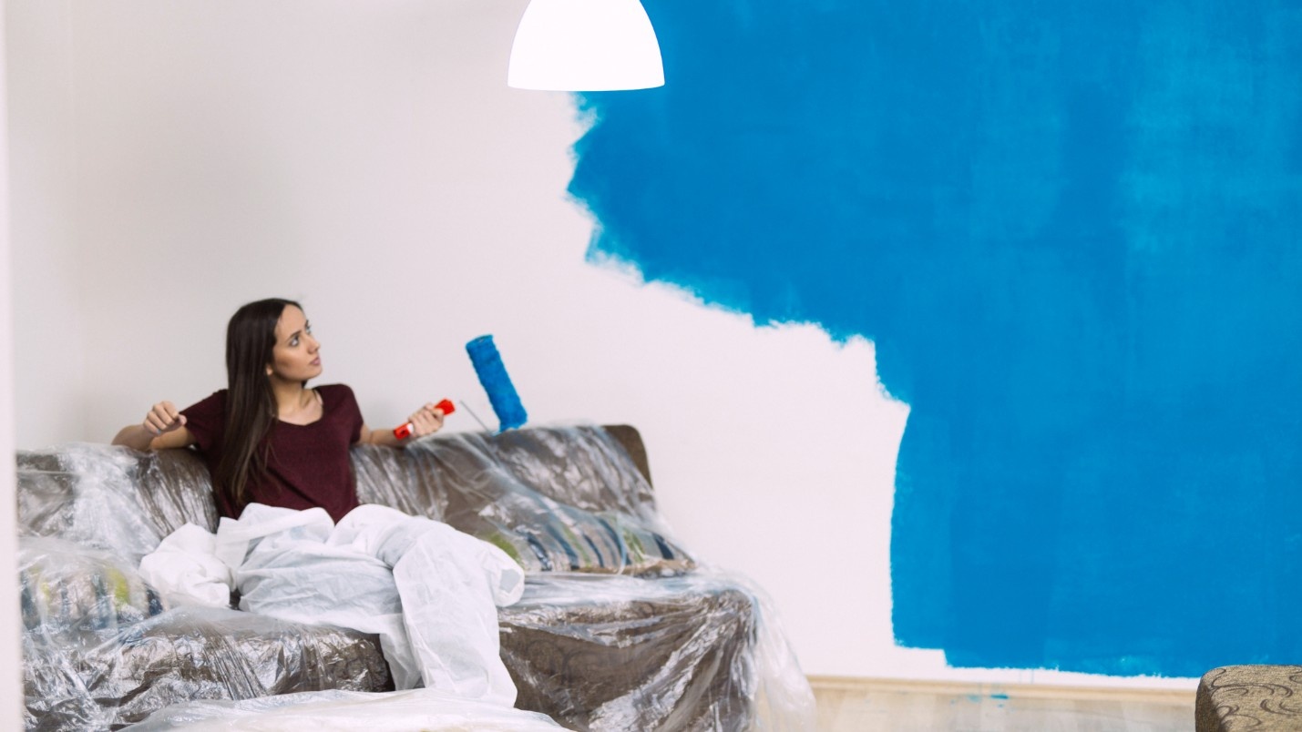 A DIY painter sits after painting half of an interior wall blue