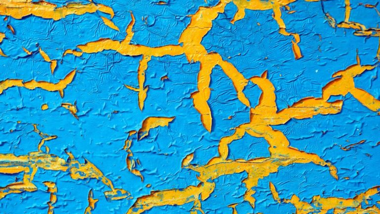 Blue paint that is cracking and peeling to reveal yellow paint underneath