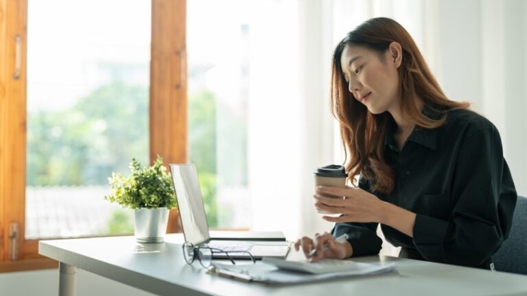 A business owner holds a coffee and works on a laptop