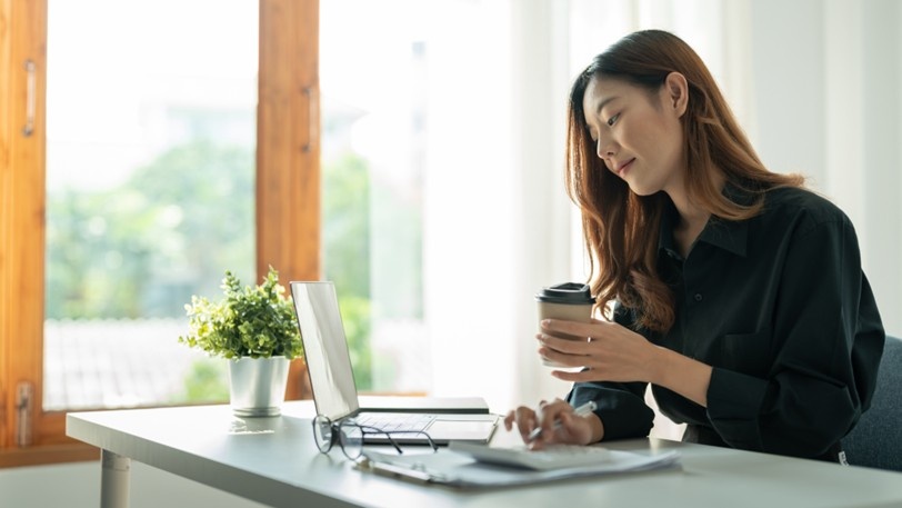A business owner holds a coffee and works on a laptop
