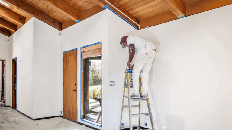 A pro home painter stands on a ladder to reach the top of an interior wall