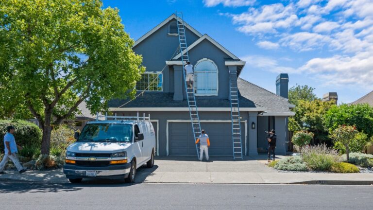 A van parked in front of a home being painted by multiple professionals