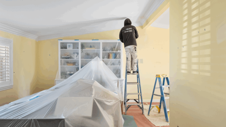 A professional painter stands on a ladder to reach the interior walls of a home