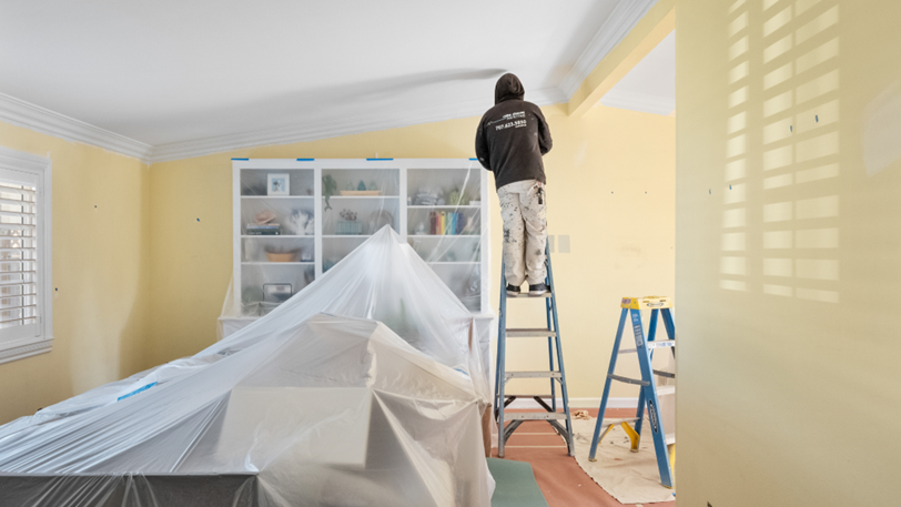 A professional painter stands on a ladder to reach the interior walls of a home