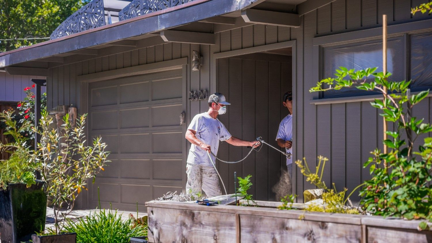 A professional painter uses a spray gun to paint the exterior of a home