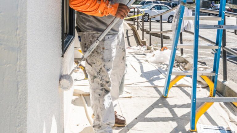 A professional painter uses a paint roller on the exterior of a business