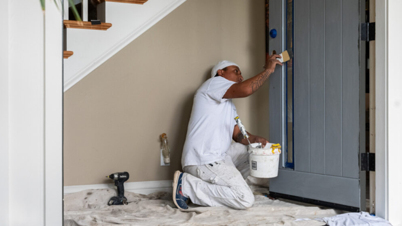 A painter uses a brush to paint grey blue details on a door