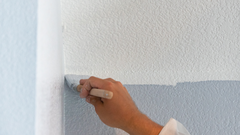A close up image of a painter using a brush to paint a wall light blue
