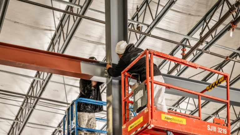 Two painters on lifts paint the metal beams of an industrial building