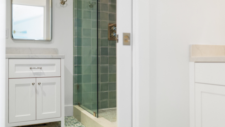 A bathroom with freshly painted cabinets in white and dark green tiles in the shower.