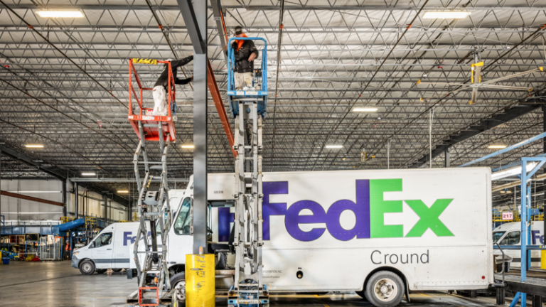 Professional painters stand on raised platforms to paint the interior of a commercial warehouse